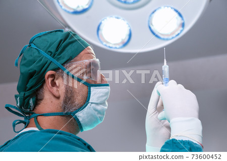 professional doctor holding general anesthetic medicine or antiviral drug vaccine needle syringe for patient before surgery in the operating room at the hospital. 73600452
