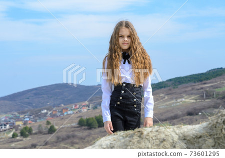Portrait of a beautiful girl of ten years old, in classic clothes against a background of blue sky and mountains, the girl looks into the frame 73601295