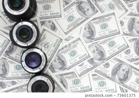 A few photographic lenses lies on the background of a lot of dollar bills. Space for text A few photographic lenses lies on the background of a lot of dollar bills. Space for text 73601375