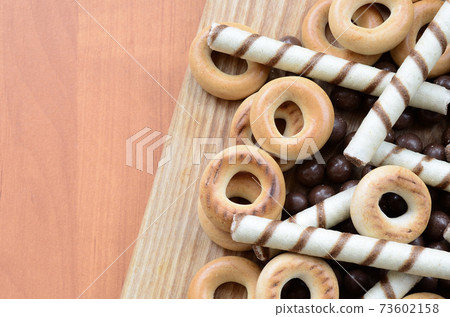 Crispy tubules, chocolate melting balls and bagels lie on a wooden surface. Mix of various sweets Crispy tubules, chocolate melting balls and bagels lie on a wooden surface. Mix of various sweets 73602158