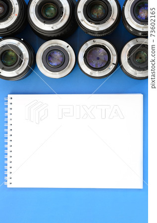 Several photographic lenses and white notebook lie on a bright blue background. Space for text Several photographic lenses and white notebook lie on a bright blue background. Space for text 73602165