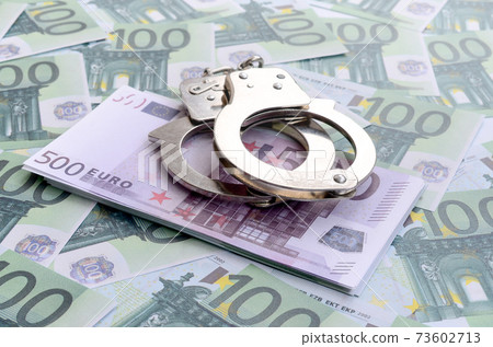 Police handcuffs lies on a set of green monetary denominations of 100 euros. A lot of money forms an infinite heap Police handcuffs lies on a set of green monetary denominations of 100 euros. A lot of money forms an infinite heap 73602713