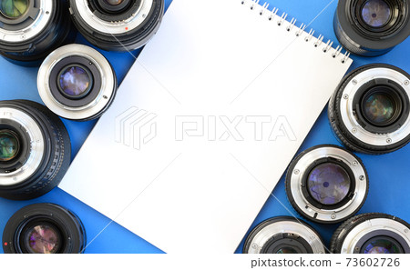 Several photographic lenses and white notebook lie on a bright blue background. Space for text 73602726