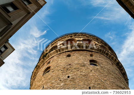 View of Galata Tower from below surrounded by classic buildings against blue sky 73602953