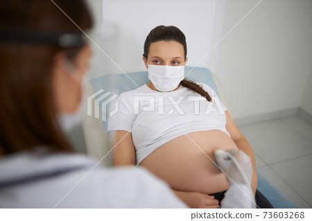 Pregnant woman in mask having ultrasound screening Pregnant woman in mask having ultrasound screening 73603268