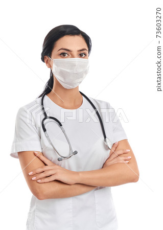 Competent doctor in uniform and face mask standing in studio Competent doctor in uniform and face mask standing in studio 73603270