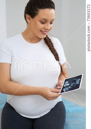 Attractive woman looking at ultrasound photos at clinic Attractive woman looking at ultrasound photos at clinic 73603272