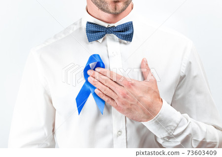 Cancer men. Awareness prostate of health in November. Hipster men in bright shirt, cyan bowtie with blue ribbon in hands on white background. Supporting people living and illness. 73603409