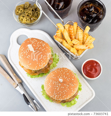Double cheese burger with caramelized onion, lettuce and jalapeno, served with french fries and soda, on white plate, top view, square format Double cheese burger with caramelized onion, lettuce and jalapeno, served with french fries and soda, on white plate, top view, square format 73603741
