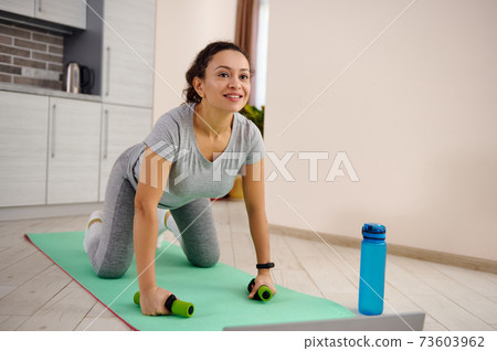 Young woman in sportswear exercising on a fitness mat during a day at home 73603962