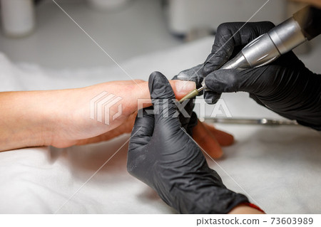 In the beauty studio, the master does hardware manicure. Removing gel polish with a cutter 73603989