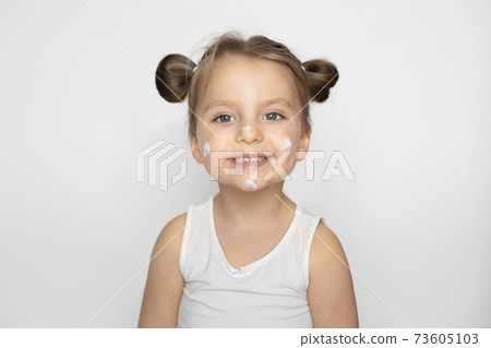 Kid cosmetics, face cream, skin care concept. Adorable smiling little girl with cream on her face, copying mom behavior, using cosmetics. Isolated on white, copy space Kid cosmetics, face cream, skin care concept. Adorable smiling little girl with cream on her face, copying mom behavior, using cosmetics. Isolated on white, copy space 73605103