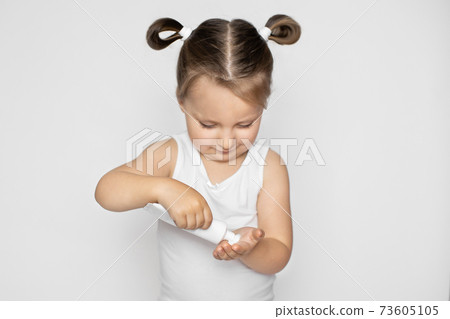 Daily children beauty product, skin care and protection, cold cream. Smiling excited blond little girl opening tube with cream and applying the cream on her hand, preparing to put it on face Daily children beauty product, skin care and protection, cold cream. Smiling excited blond little girl opening tube with cream and applying the cream on her hand, preparing to put it on face 73605105
