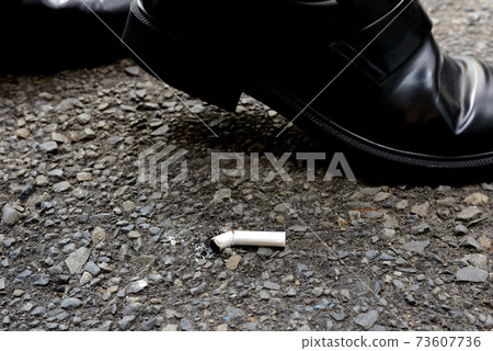 At the feet of a businessman walking by a littered cigarette 73607736
