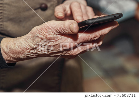 Old woman's wrinkled hands hold a modern mobile phone Old woman's wrinkled hands hold a modern mobile phone 73608711