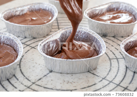 Making sweets at home, pouring chocolate cake dough for Valentine's Day into a heart-shaped cup 73608832