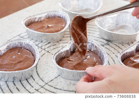 Making sweets at home, pouring chocolate cake dough for Valentine's Day into a heart-shaped cup Making sweets at home, pouring chocolate cake dough for Valentine's Day into a heart-shaped cup 73608838