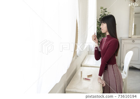 A woman looking in the mirror and applying rouge (lipstick) A woman looking in the mirror and applying rouge (lipstick) 73610194
