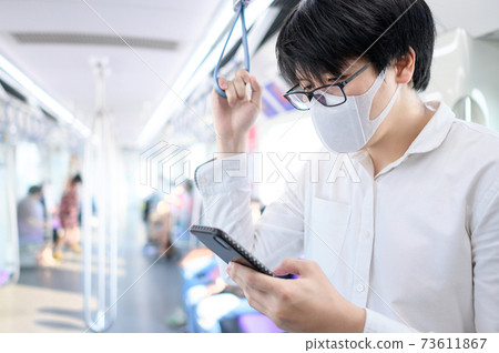 Asian man wearing mask using phone on skytrain Asian man wearing mask using phone on skytrain 73611867