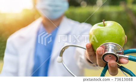 World health day, an apple a day keeps the doctor away concept for health benefit by eating high nutritious clean food and healthy nutritional diet with doctor handling green apple giving to patient 73613088