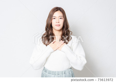 一個年輕的女人站在白牆前,把她的手放在她的胸部 一個年輕的女人站在白牆前,把她的手放在她的胸部 73613972