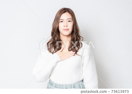 一個年輕的女人站在白牆前，把她的手放在她的胸部 73613973