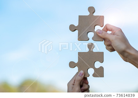 Woman hands connecting couple puzzle piece against sunrise effect, businesswoman holding wood jigsaw with sunset background. Business solutions, target, success, goals and strategy concepts 73614839
