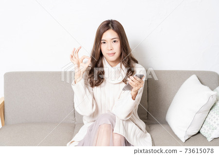 一個年輕的女人坐在客廳裡的沙發上,操作智能手機 一個年輕的女人坐在客廳裡的沙發上,操作智能手機 73615078