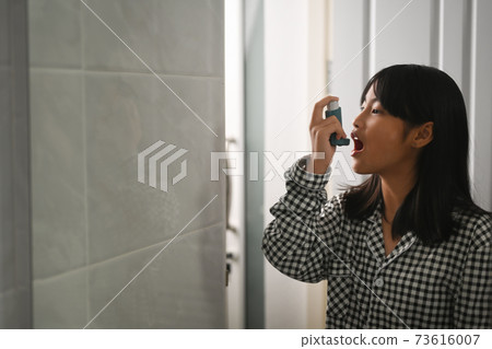 Young Asian asthma patient girl using asthma inhaler for treating shortness of breath and wheezing. Young Asian asthma patient girl using asthma inhaler for treating shortness of breath and wheezing. 73616007