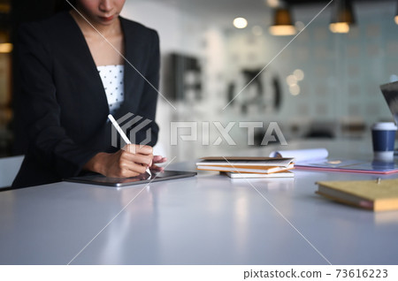 Close up view of businesswoman holding stylus pen writing on digital tablet at meeting table. Close up view of businesswoman holding stylus pen writing on digital tablet at meeting table. 73616223