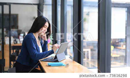 Cheerful young female freelancer working with tablet computer at comfortable workstation. Cheerful young female freelancer working with tablet computer at comfortable workstation. 73616298