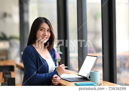 Attractive young woman designer sitting at her workstation and smiling to camera. Attractive young woman designer sitting at her workstation and smiling to camera. 73616299