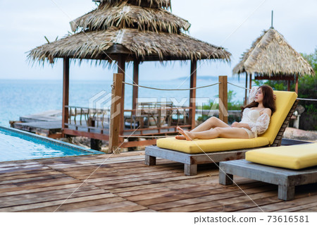 woman relax on deck chair in pool with sea background 73616581