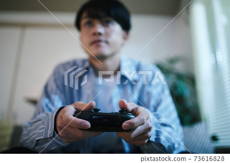 A man holding a game controller while relaxing on the sofa 73616828