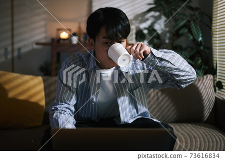 A man who concentrates on the computer and drinks on the sofa 73616834