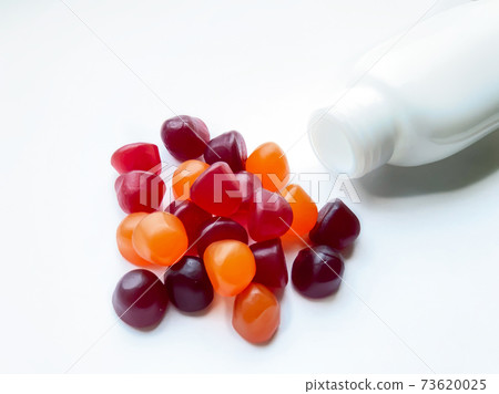 Group of red, orange and purple multivitamin gummies with the bottle isolated on white background. Healthy lifestyle concept. 73620025