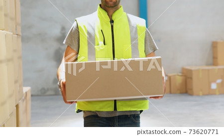 Warehouse worker carrying cardboard box in the warehouse 73620771