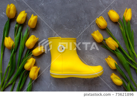Yellow tulips and yellow rubber boot on grey background. Trendy color 2021. 73621896