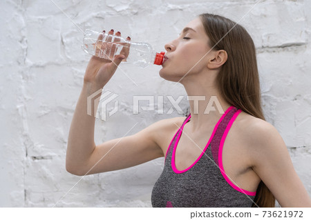 Young athlete woman takes a break drinking water from plastic bottle. Young woman drinking water after working out in the gym, health and sport concept 73621972
