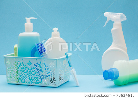 Bottles of dishwashing liquid in basket, sponges and brushes on blue background. 73624613