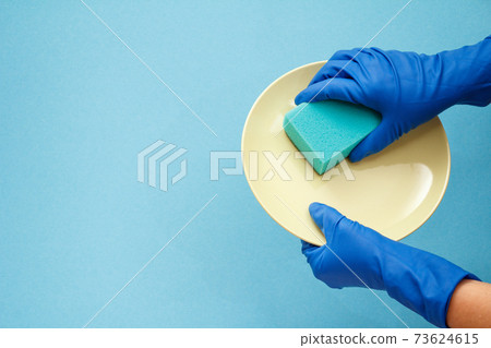 Women's hands in protective gloves with sponge and plate on blue background. Women's hands in protective gloves with sponge and plate on blue background. 73624615