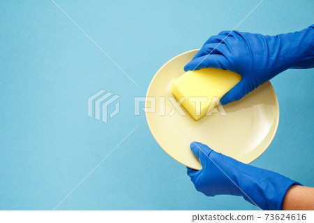 Women's hands in protective gloves with sponge and plate on blue background. Women's hands in protective gloves with sponge and plate on blue background. 73624616
