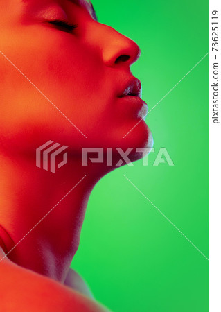 Beautiful east woman close up portrait isolated on green background in red neon light 73625119