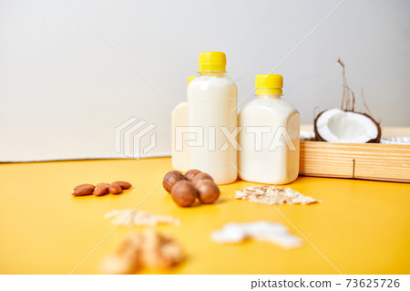 Alternative types of vegan milks in bottles on a yellow background 73625726