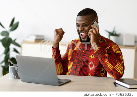 Overjoyed African Businessman In Traditional Clothes Celebrating Success At Workplace In Office Overjoyed African Businessman In Traditional Clothes Celebrating Success At Workplace In Office 73626323