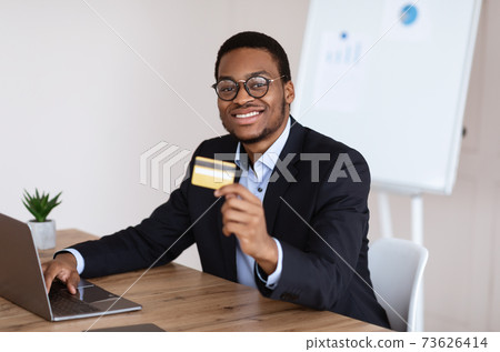 Happy black businessman using laptop, recommending credit card Happy black businessman using laptop, recommending credit card 73626414