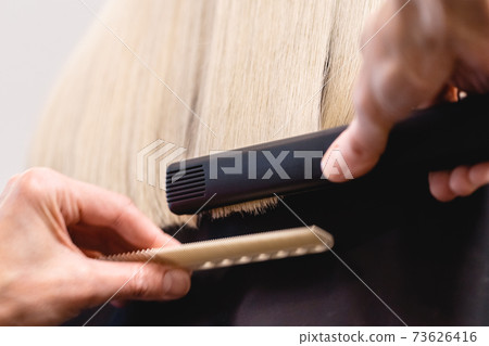 Hairdresser straightens blonde hair with flat iron Hairdresser straightens blonde hair with flat iron 73626416