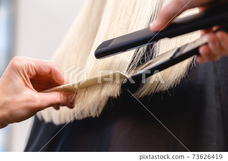 Hairdresser straightens blonde hair with flat iron Hairdresser straightens blonde hair with flat iron 73626419