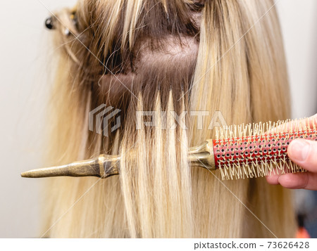 Blonde hair extensions procedure in beauty salon 73626428