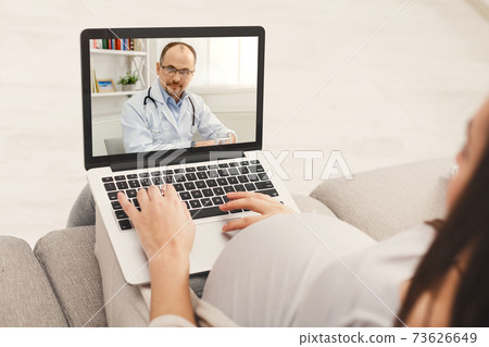Online medical care during pregnancy. Young expectant woman consulting her prenatal doctor on laptop from home 73626649